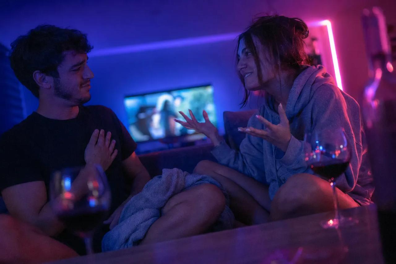 Pár sedící spolu na gauči, smějí se při hraní hry 21 otázek během rande večera