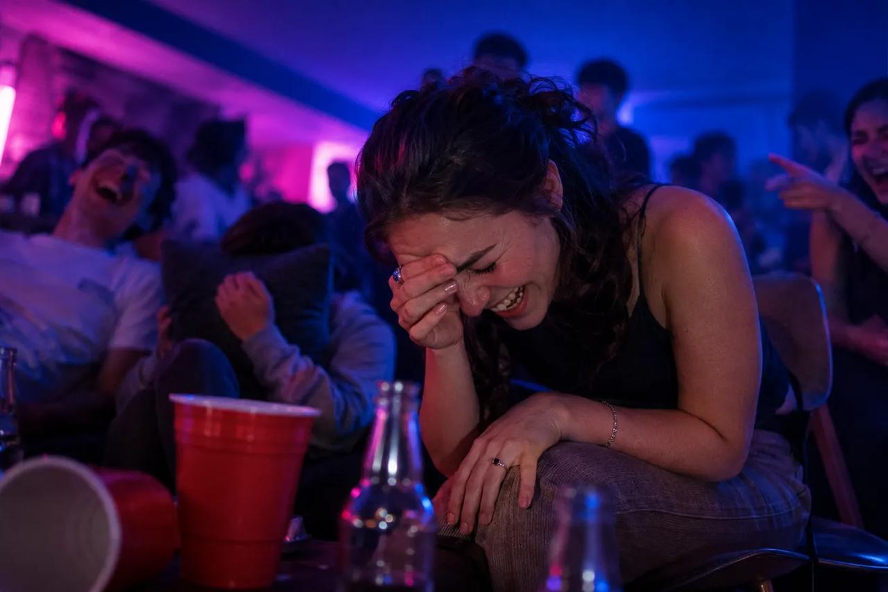 Amigos rindo muito numa festa enquanto uma pessoa na cadeira quente responde a uma pergunta engraçada e constrangedora
