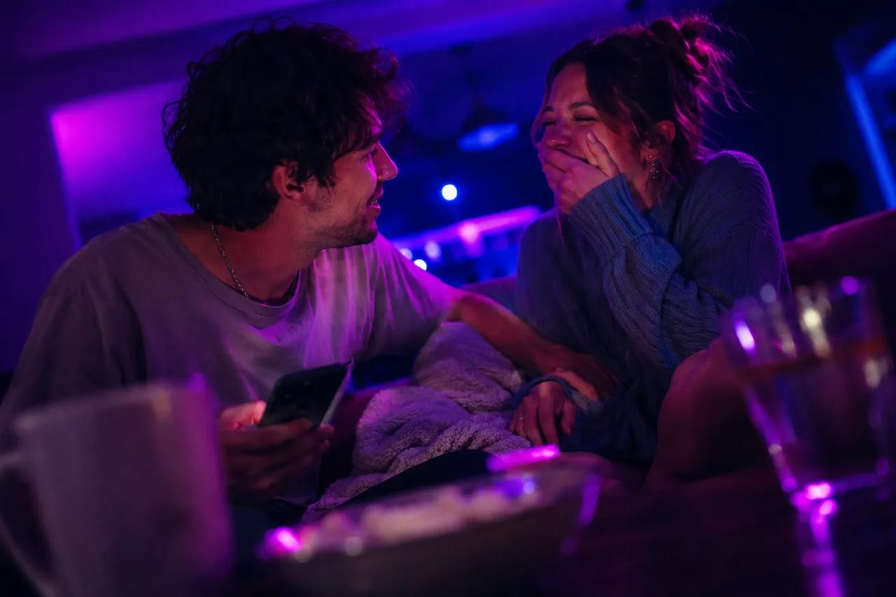 Et par sidder sammen på en sofa, griner og hygger sig med en sjov quiz på deres date night