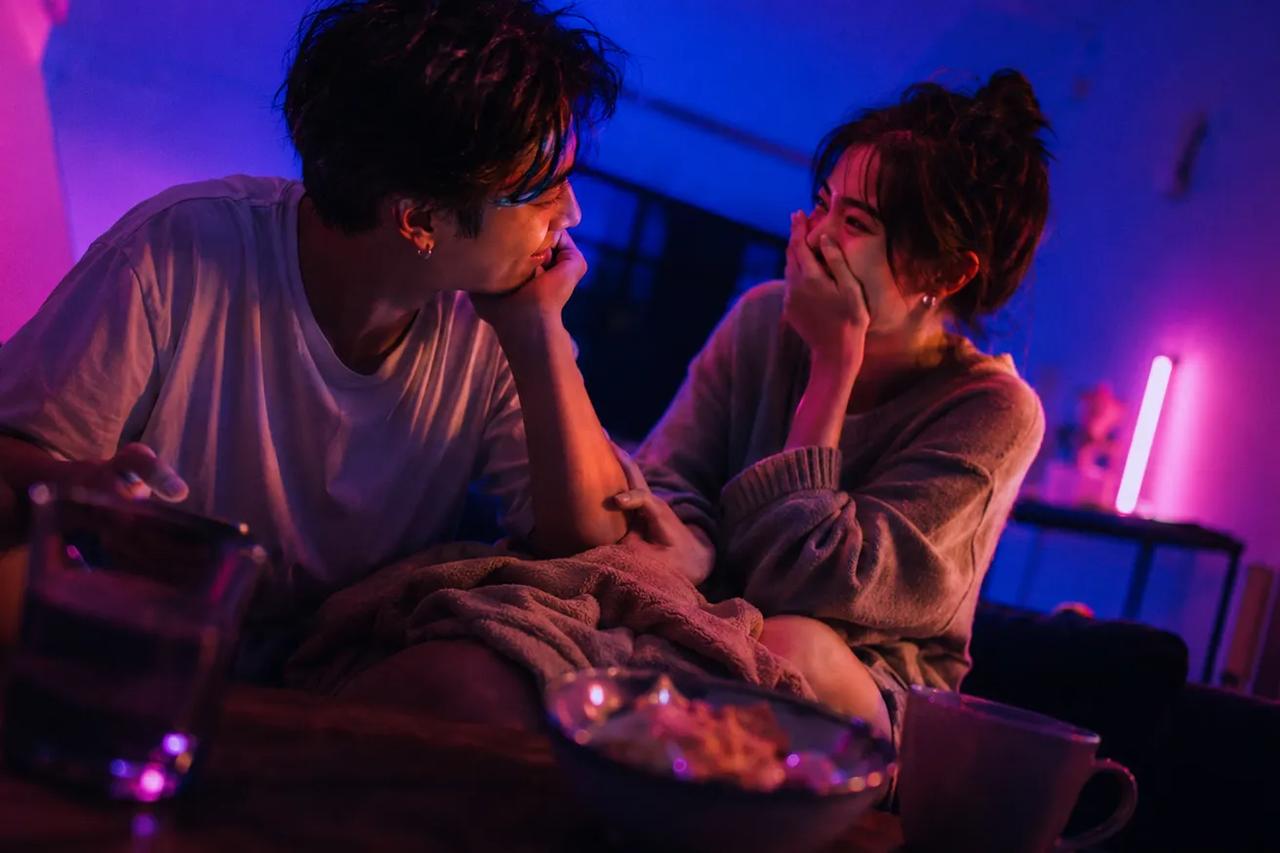 คู่รักนั่งหัวเราะด้วยกันบนโซฟา เล่นควิซทายใจสนุกๆ ในคืนเดทไนท์