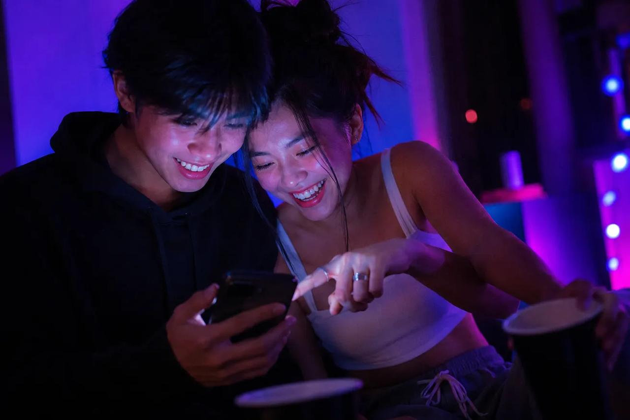 คู่รักกำลังเล่นแอปเกมปาร์ตี้ TOZ บนมือถือระหว่างเล่นเกมวงเหล้าแบบสองคน