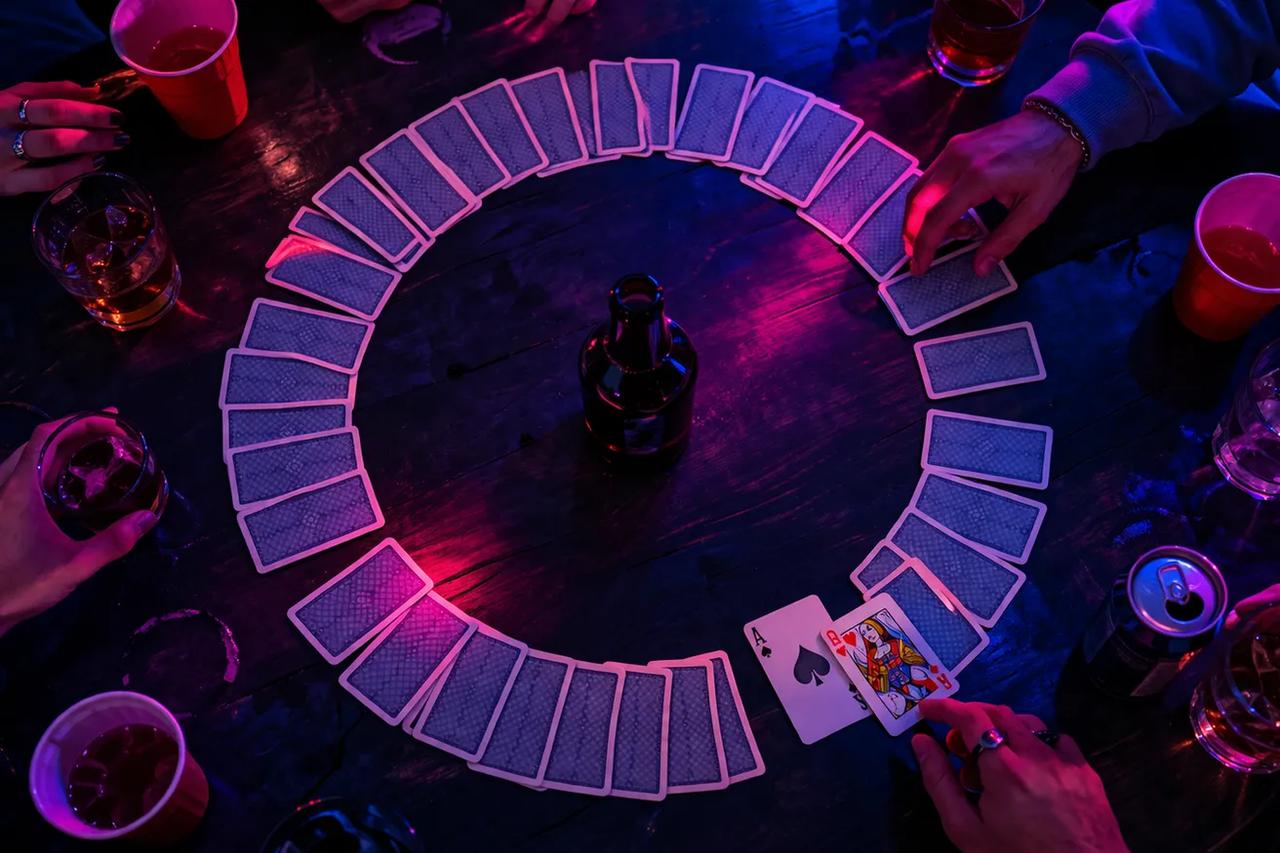 Un grupo de amigos sentados en círculo jugando el juego de beber Waterfall con cartas esparcidas sobre una mesa